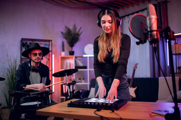 Caucasian man playing electronic drums while woman mixing sound on equalizer. Talented duo of musicians working on new song at professional music studio.