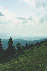 View from top mountain to wooded mountain landscape against background sky covered white-gray dense clouds.