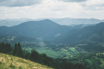 View from top mountain to wooded mountain landscape against background sky covered white-gray dense clouds.