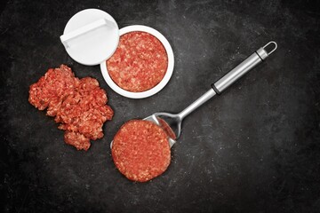 Patty Press and Raw Burgers on Wooden Board. Plastic Burger Stuffer with Grill Tools, Top View. Beef and Pork Mince Patties on Rustic Black Background, Overhead View.