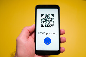 A smartphone with electronic immune digital health passport, Covid pass with QR code in mans hand on the yellow background.