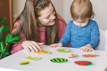 Young mother and one and a half year old girl collects puzzles. Psychomotor skills and the development of logical thinking