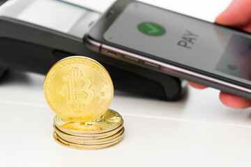 Golden bitcoin on the background of contactless payment by mobile phone.