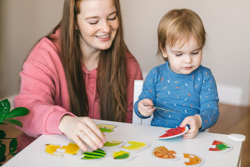 Young mother and one and a half year old girl collects puzzles. Psychomotor skills and the development of logical thinking