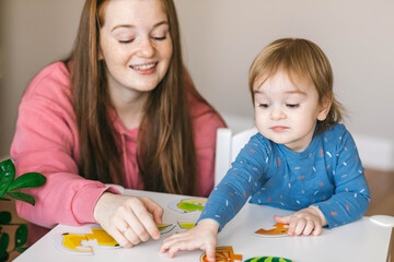 Young mother and one and a half year old girl collects puzzles. Psychomotor skills and the development of logical thinking