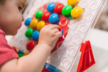 Fototapeta na wymiar Two-year-old child plays with mosaics, fine motor skills development