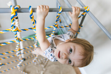 Two-year-old child crawling on the rope net of a home sports complex, the development of gross...