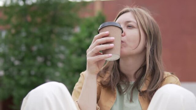 Close-up, a fashionable female tourist drinks coffee in the park in the summer.