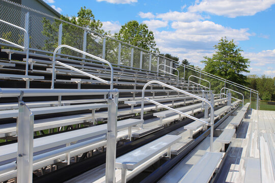 Empty metal bleachers during a sunny spring day with green trees and a blue sky in the background