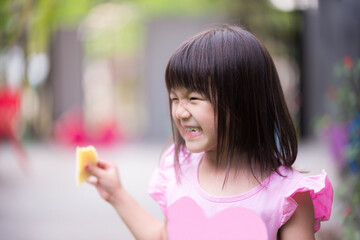 Portrait of Asian cute girl smile and laughing during eating fruit. Kid holding ripe mango. Happy child wearing pink shirt. Children aged 5 - 6 years old.