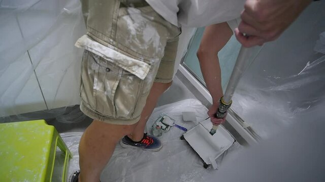Painter Dipping Paint Roller In Paint Pan In Bathroom Covered In Plastic 