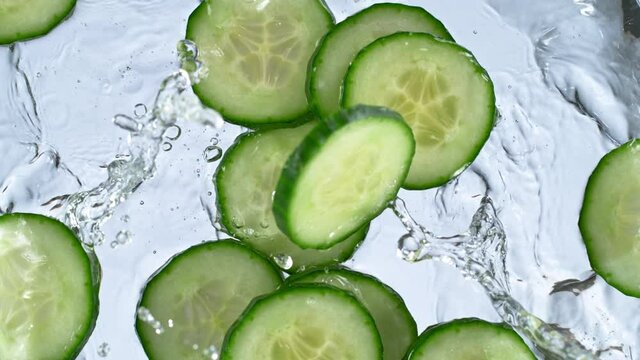 Super slow motion of falling fresh cucumber slices with water splashing during impact, 1000 fps.