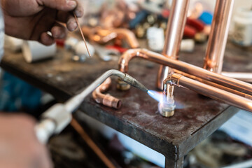 Close up on hands of unknown industrial worker plumber with central heating copper pipes welding...