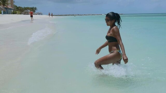 Palm Beach Aruba, Amazing tropical beach with palm trees entering the ocean against azur ocean, gold sand, and blue sky. woman walking at a white beach, mid age 