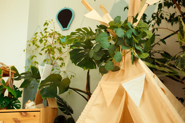 interior of a children's room or recreation area: a wigwam with soft pillows, a wooden nightstand made of environmentally friendly materials. plastic plants to decorate the space © skeronov