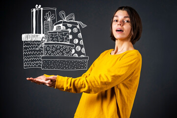 A young funny girl in a yellow sweater enthusiastically catches a bunch of gifts with a joyful...