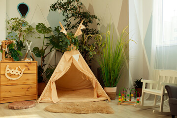 interior of a children's room or recreation area: a wigwam with soft pillows, a wooden nightstand made of environmentally friendly materials. plastic plants to decorate the space © skeronov