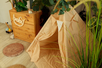 interior of a children's room or recreation area: a wigwam with soft pillows, a wooden nightstand made of environmentally friendly materials. plastic plants to decorate the space © skeronov