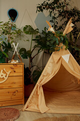 interior of a children's room or recreation area: a wigwam with soft pillows, a wooden nightstand made of environmentally friendly materials. plastic plants to decorate the space © skeronov