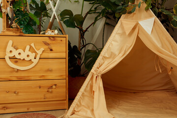 interior of a children's room or recreation area: a wigwam with soft pillows, a wooden nightstand made of environmentally friendly materials. plastic plants to decorate the space © skeronov