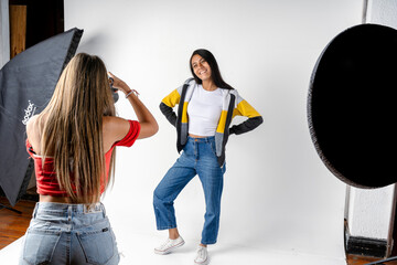 Photo session of a model and a woman photographer in a photography studio with flashes and a white background. Fashion concept. - obrazy, fototapety, plakaty
