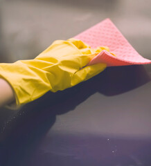 A female hand in a yellow rubber glove holds a damp pink sponge and wipes the surface. The woman is cleaning the house.