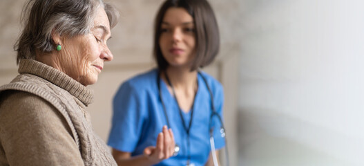 Obraz premium Young nurse is caring for an elderly 80-year-old woman at home, helping her and giving her treatment recommendations. Happy retired woman and trust between doctor and patient. Medicine and healthcare.