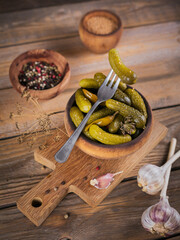 Gherkins, pickled cucumber on a fork, bowl of marinated vegetables on rustic wooden background