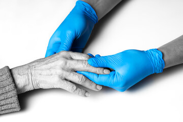 Obraz premium Doctor's hands in a blue gloves holds the hands of an elderly woman, a patient. Handshake, caring, trust and support. Medicine and healthcare.