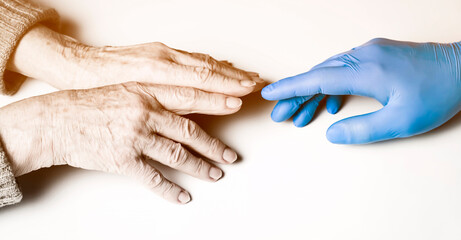 Fototapeta premium A doctor's hands in a blue gloves holds the hands of an elderly woman, a patient. Handshake, caring, trust and support. Medicine and healthcare.