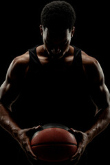 Basketball player holding a ball against black background. Serious concentrated african american man