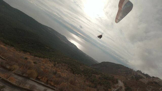 Active couple flying on paraglider over nature seascape with cloudy sky at sunset aerial shot. People on paraplane enjoy extreme sports Black sea and mountain shooting from fpv high speed racing drone