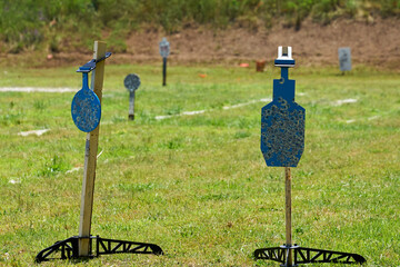 AR500 Steel gong and silhouette Shooting Targets on stands sitting on a grass field at a shooting range.