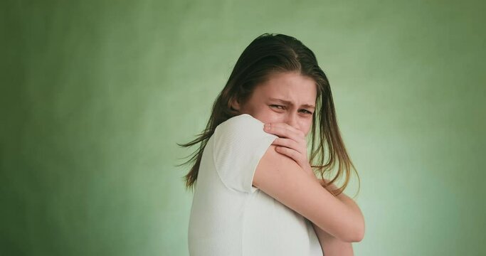 Crying young woman hugs herself and closes face with palms