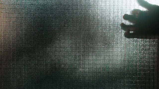 Beautiful abstract shadow on the glass wall. Silhouette of a man's hand fingering on the glass with his fingers. Moving silhouettes on a window.