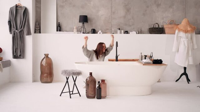 funny brunette woman moves around bath in bathroom dancing in pajamas and bathrobe at home celebrating freedom joyful day