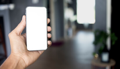 Hand holding black smartphone with white screen mockup and room with copy space background, Mobile phone frameless design concept.