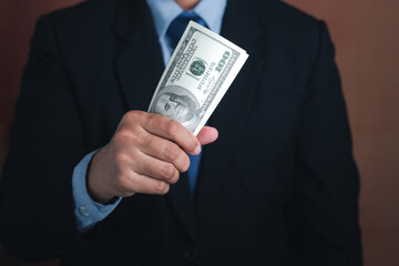 Hand of a businessman holding US dollars while standing with a brown background. Personal loans or business loans. Space for text. Close-up photo. Business and finance concept