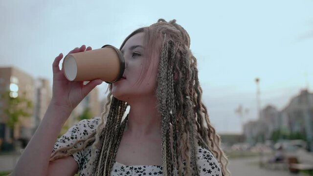 Young girl with dreadlocks with coffee walks on the street