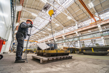 Worker in mask and helmet works with cargo crane in industrial factory workshop for woodwork.