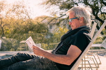 older man reads outdoors with sun and pool