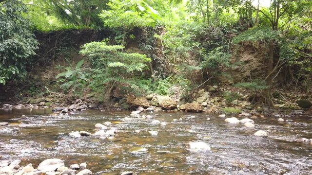 Crystal clear white water flowing downstream over stones and pebbles which make up the riverbed. Wang Takrai stream in Namtok Wang Ta Krai nature park in Nakhon Nayok, Thailand.