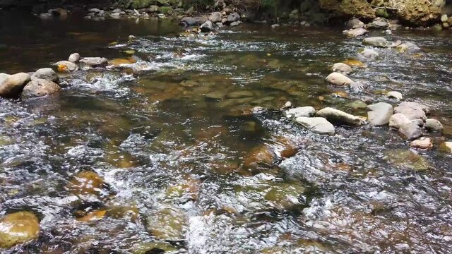 Crystal clear white water flowing downstream over stones and pebbles which make up the riverbed. Wang Takrai stream in Namtok Wang Ta Krai nature park in Nakhon Nayok, Thailand.