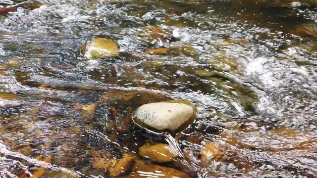 Crystal clear white water flowing downstream over stones and pebbles which make up the riverbed. Wang Takrai stream in Namtok Wang Ta Krai nature park in Nakhon Nayok, Thailand.