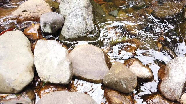 Crystal clear white water flowing downstream over stones and pebbles which make up the riverbed. Wang Takrai stream in Namtok Wang Ta Krai nature park in Nakhon Nayok, Thailand.