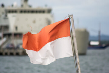 Indonesian national flag with battleship in the background.