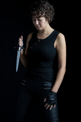 An urban fantasy woman wearing a black singlet and leather pants and standing against a black backdrop