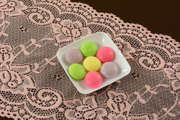 Multicolor soda pop mint candies small white candy dish on pink  lace table runner on brown...