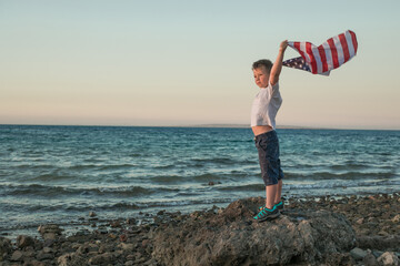 Little boy lets the american flag fly in his hands on the wind at the Sea. Patriotic family celebrates usa independence day on 4th of July.