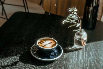 Cup of cappuccino coffee on black wooden table at cofffe shop. Lights and shadows, food drink...